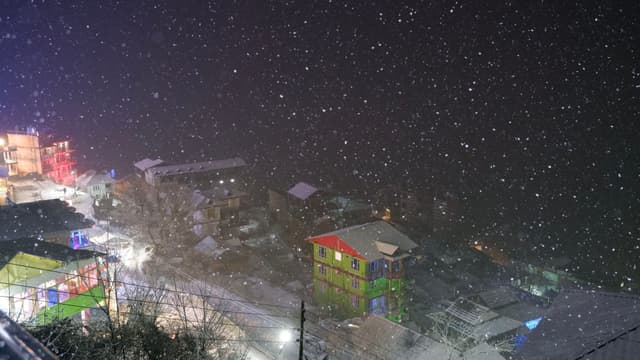 A snowy night scene in a town with colorful buildings and illuminated streets